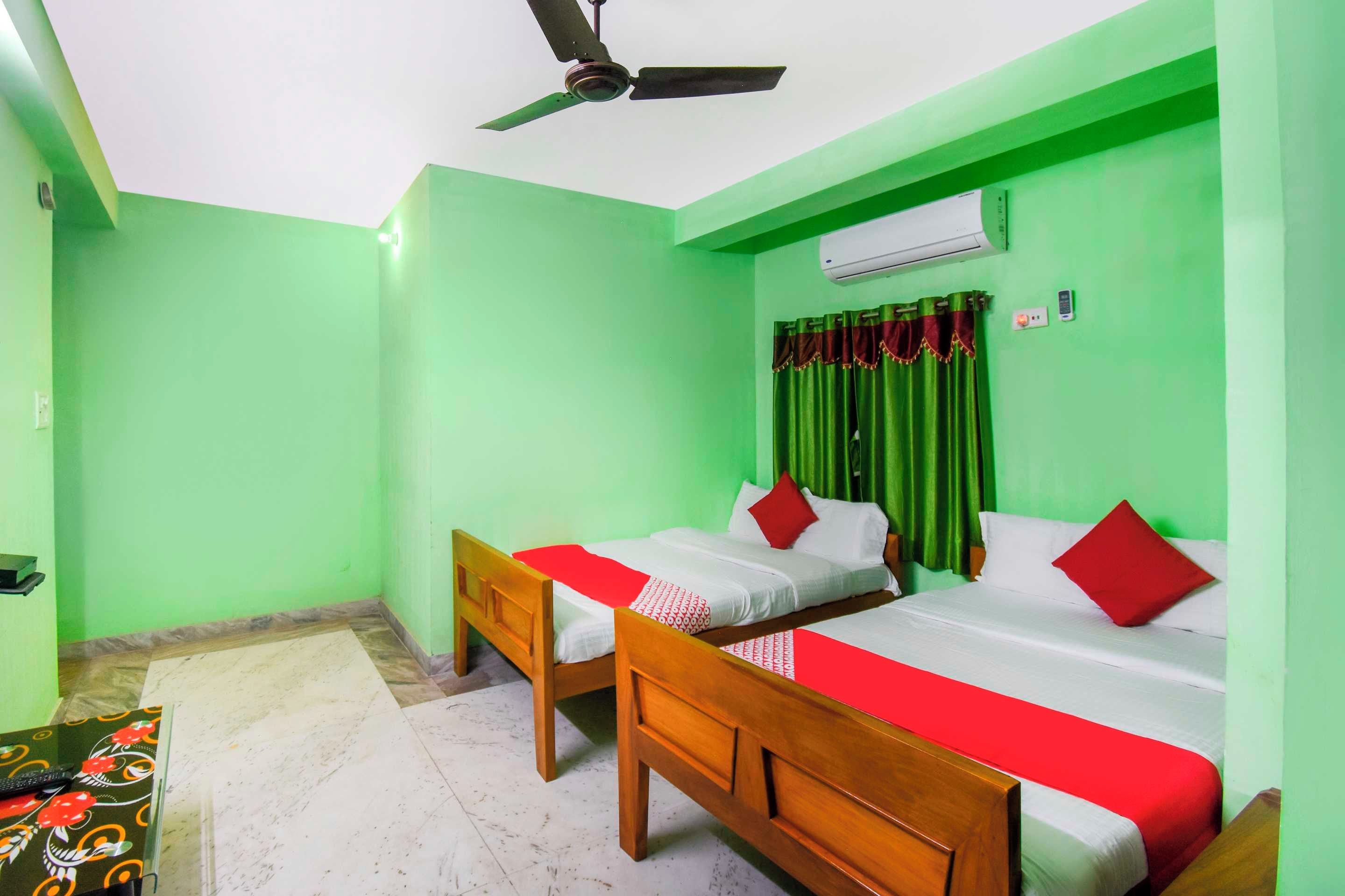Una habitación con dos camas, ventilador de techo, aire acondicionado y una pared verde.