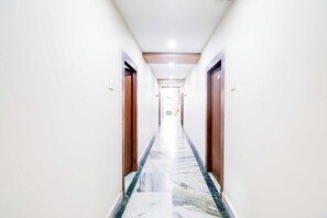 Corredor de hotel com piso de mármore, portas de madeira e teto com iluminação embutida.
