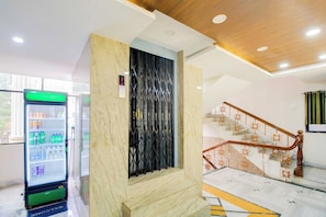 Un interior moderno con un pilar de mármol, una escalera con barandales ornamentados y un expendedor.