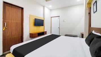Habitación de hotel con una cama grande, un armario de madera, un televisor en la pared y una puerta.
