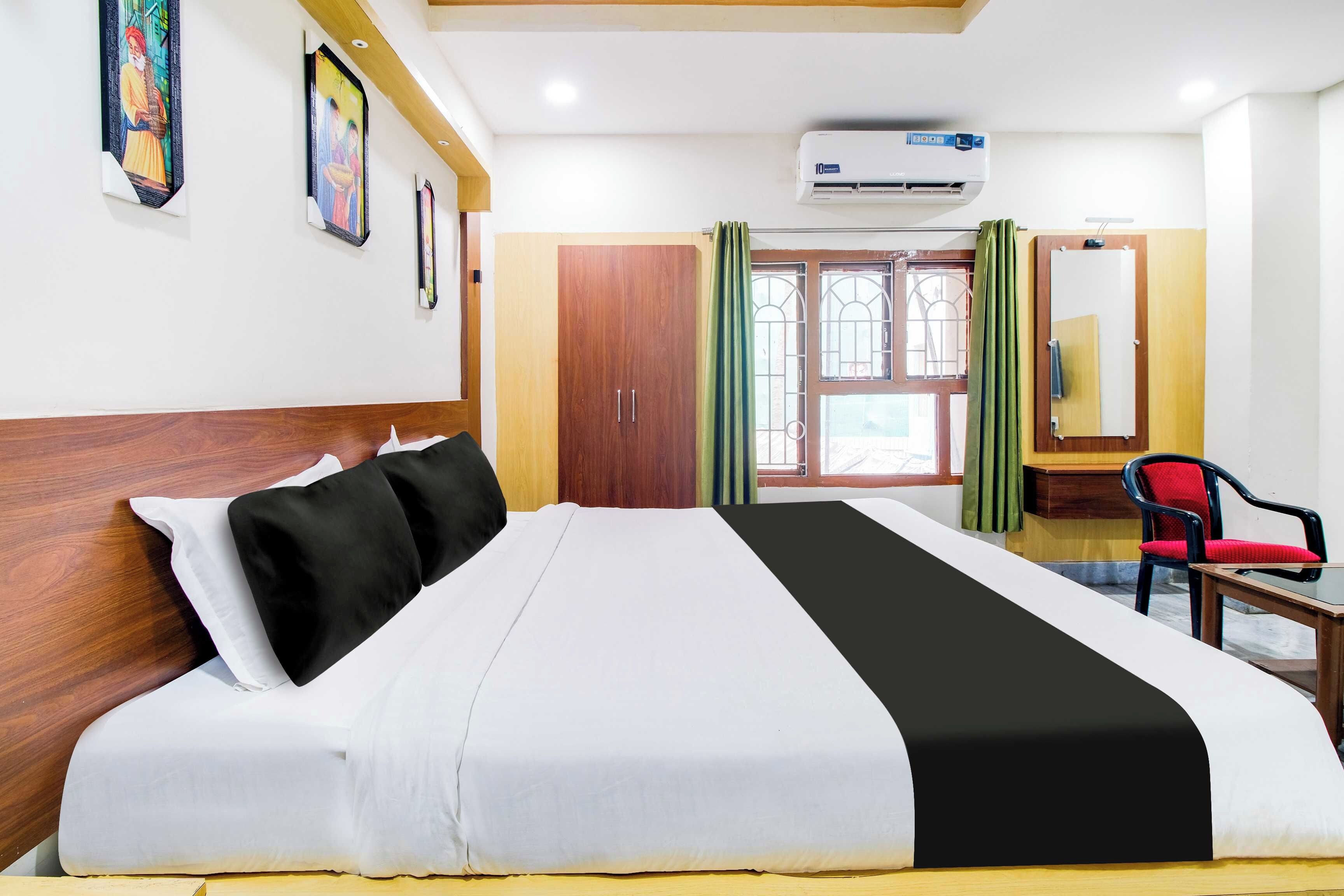 A hotel room with a bed, a desk, a chair, an air conditioner, and a window with curtains.