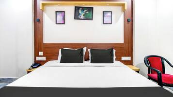 A hotel room with a wooden headboard, two black pillows, a white bedspread, and a single red chair.