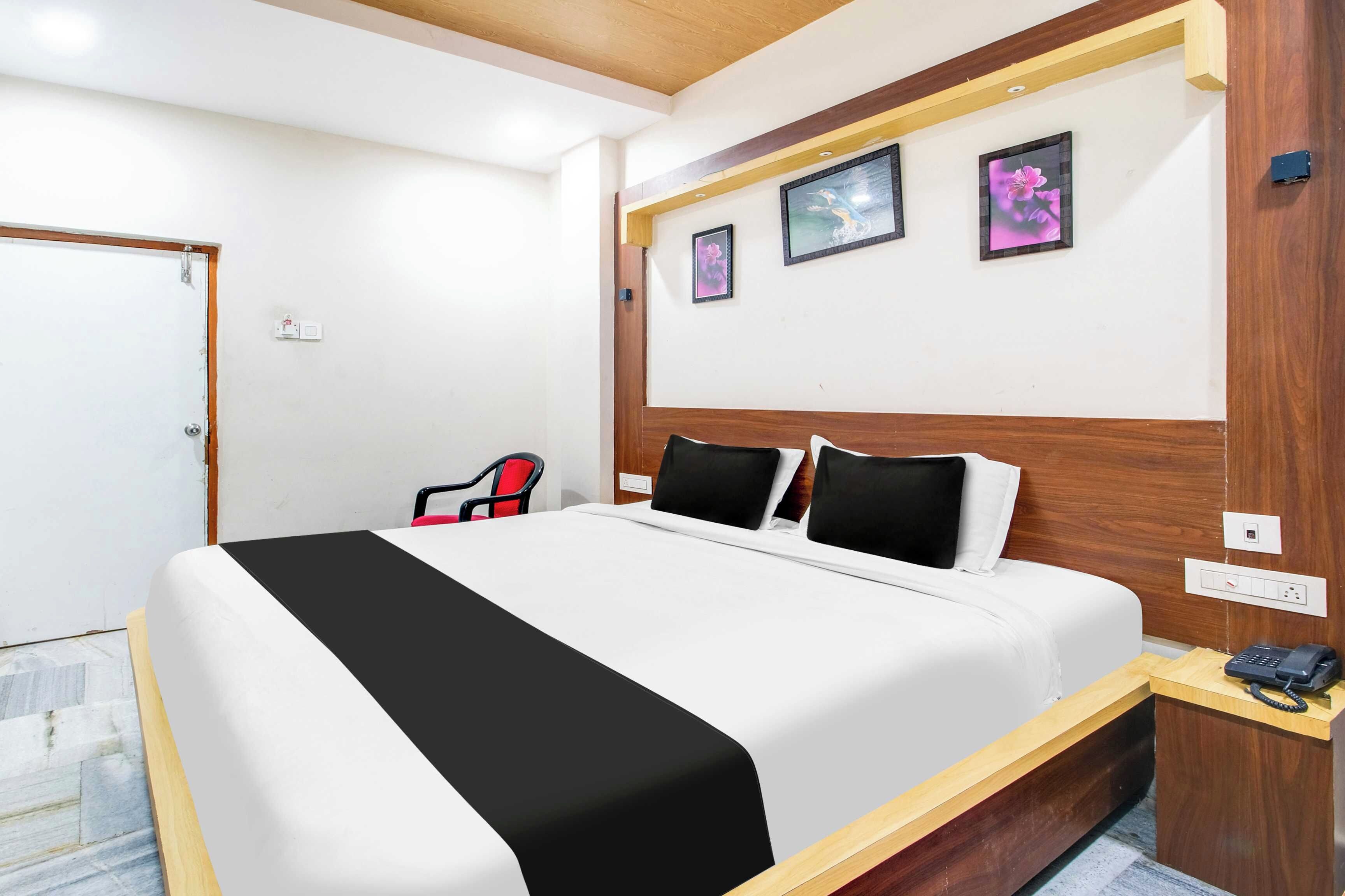 A hotel room with a bed, a desk with a telephone, and three framed pictures on the wall.