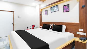 A hotel room with a bed, a desk with a telephone, and three framed pictures on the wall.
