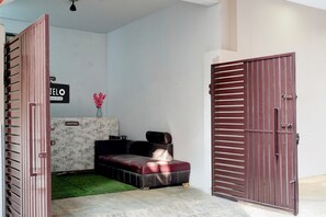 A reception area with a sofa, a small table with a vase, and a closed door. - Hotel O Sector 23 Udyog Vihar (Gurugram)
