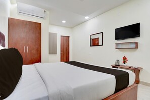 A hotel room with a bed, wardrobe, television, and a small table with a vase and remote control. - Hotel O Magunta Layout Nellore (Nellore)