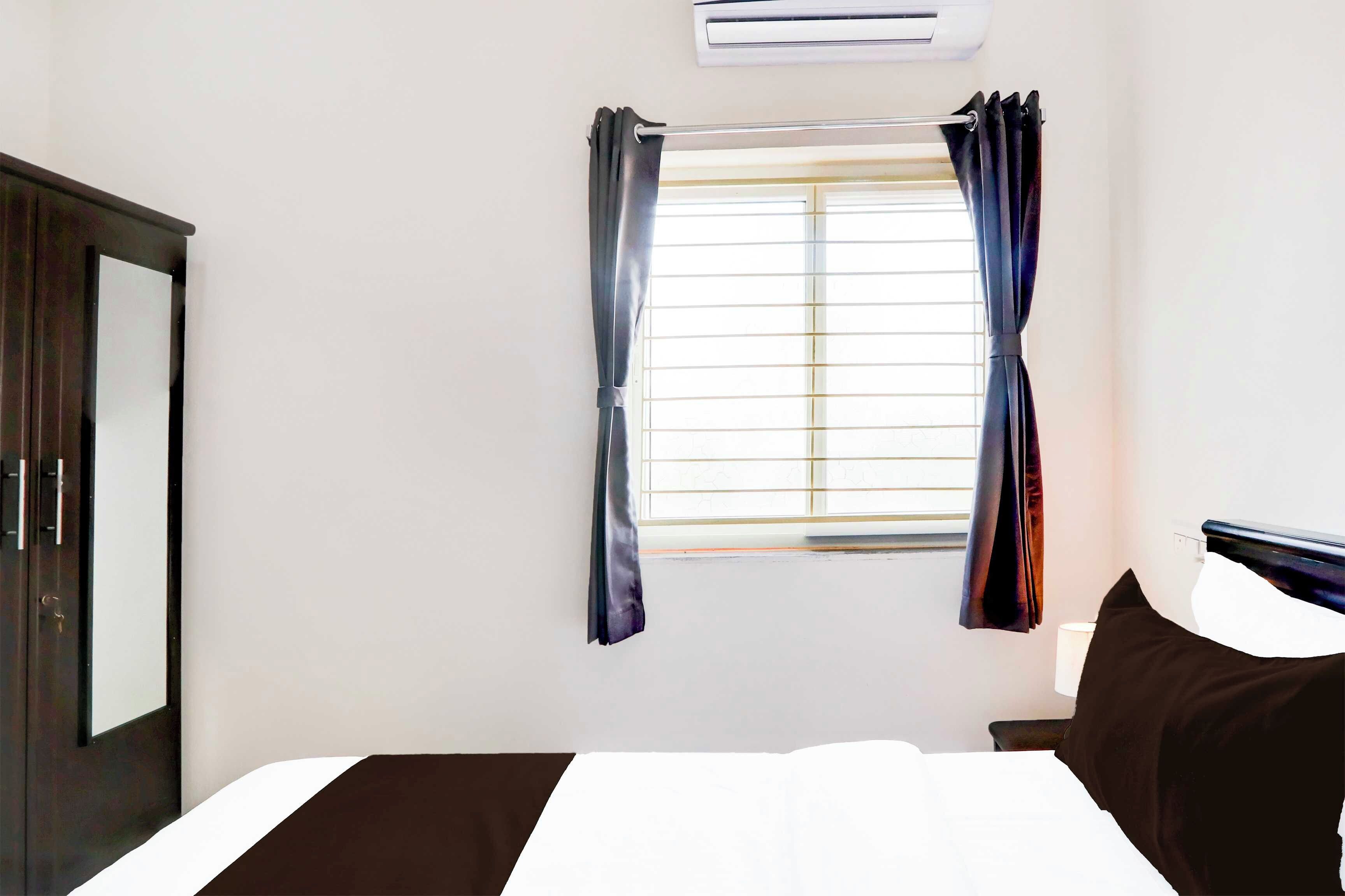 Quarto de hotel com cama, janela com cortinas, ar condicionado e guarda-roupa escuro.