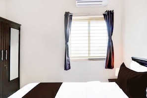 Una habitación de hotel con cama, ventana con cortinas, aire acondicionado y un armario de color oscuro.
