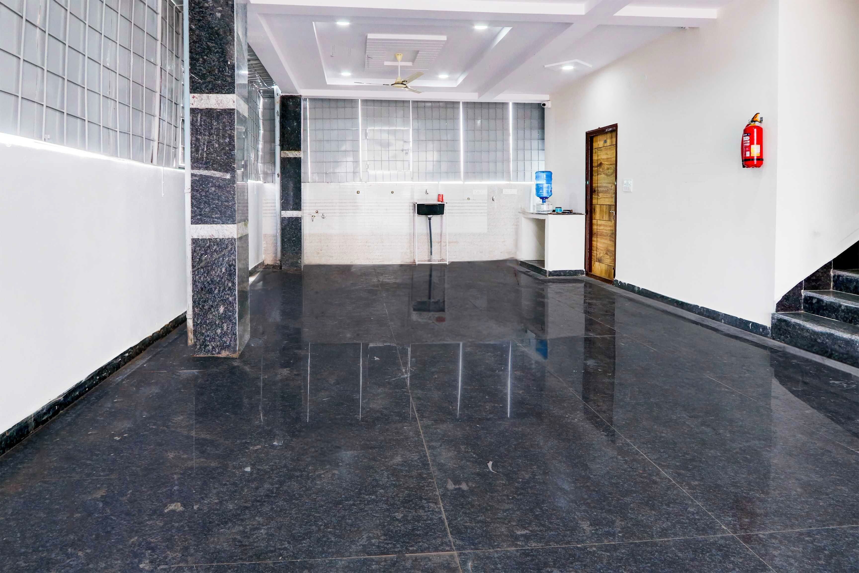 A clean, modern lobby with a marble floor, a water dispenser, a fire extinguisher, and a ceiling fan.