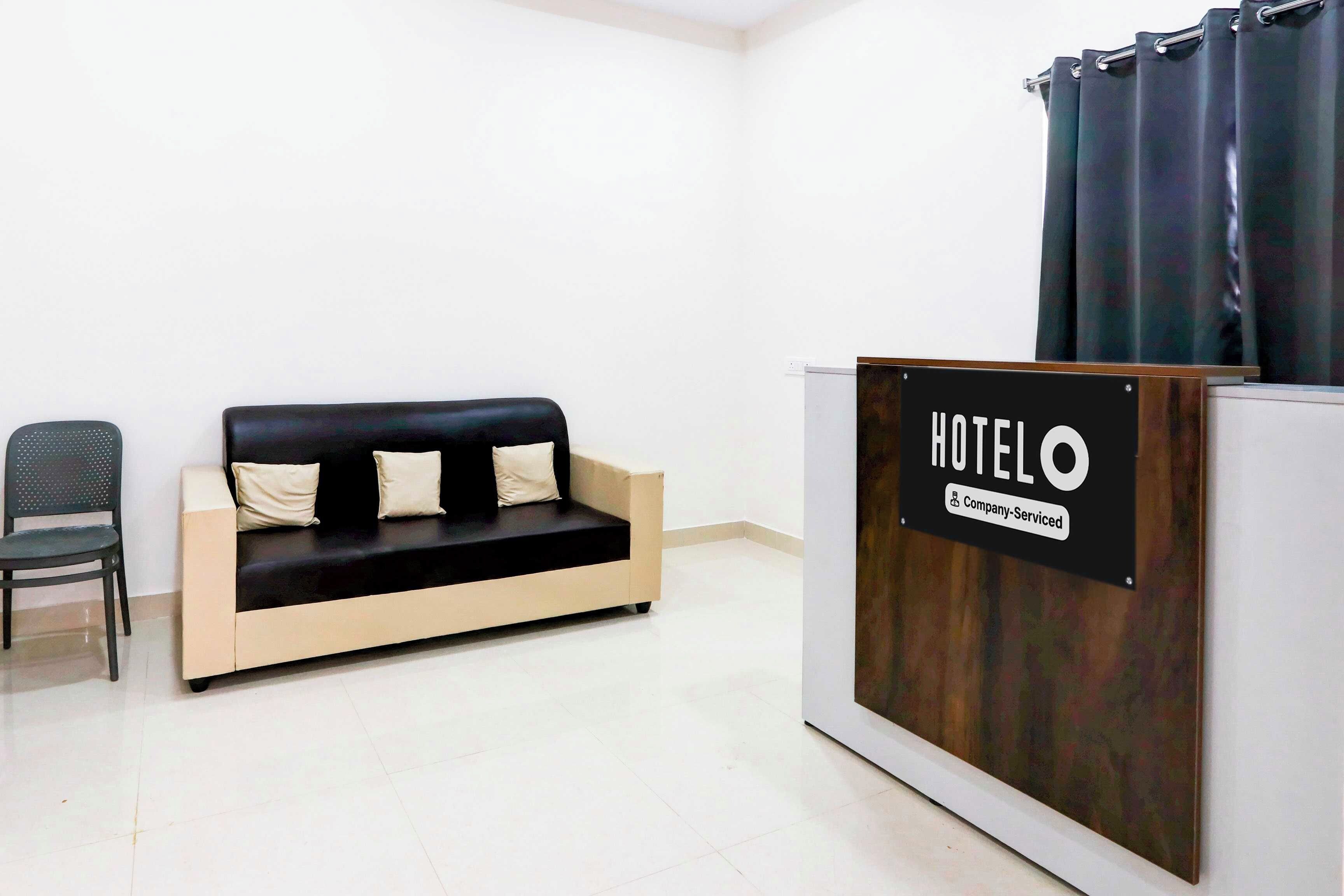 A hotel reception area with a reception desk, a black sofa with cushions, and a chair.