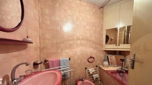 A bathroom with a pink sink, a mirror, and a cabinet with toiletries. - Vrbo Property (Deux-Grosnes)