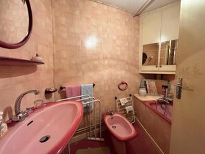 Een badkamer met een roze wastafel, een spiegel en een kastje met toiletartikelen.