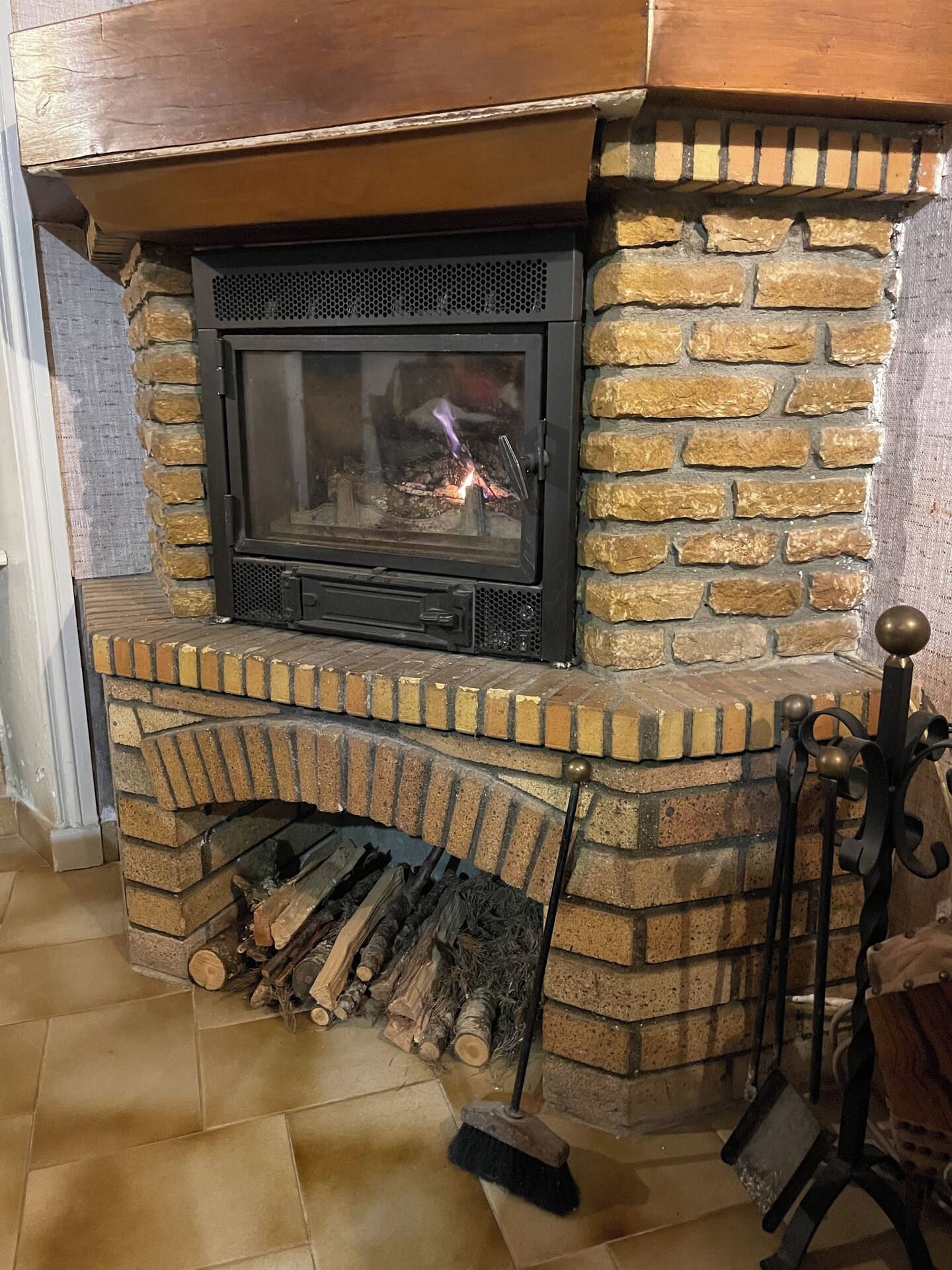 Une cheminée avec un manteau en pierre et un foyer en métal, et des bûches rangées en dessous.