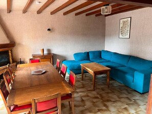 A cozy room with a wooden dining table, red cushioned chairs, a blue sofa, and a fireplace.