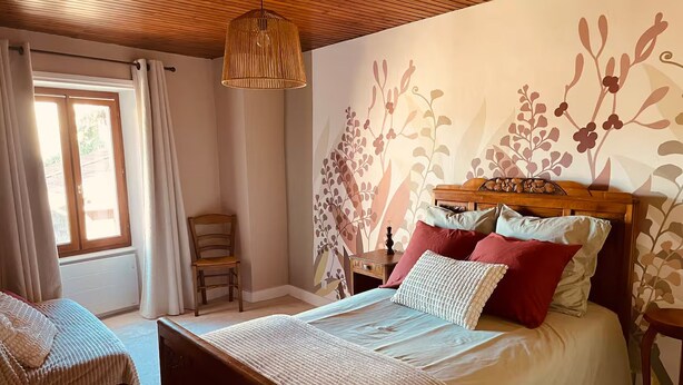 A bedroom with a bed, a chair, a nightstand, and a hanging light fixture. - Vrbo Property (Deux-Grosnes)