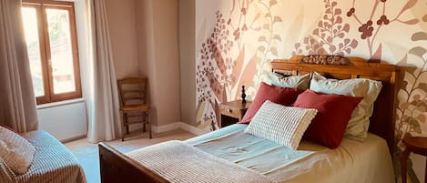 A bedroom with a bed, a chair, a nightstand, and a hanging light fixture.