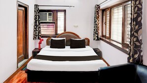 Een slaapkamer met een bed, nachtkastje, stoel, raam met gordijnen en een airconditioning.