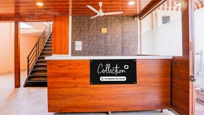 A reception desk with a wooden finish, a ceiling fan, and a patterned wall in the background. - Collection O Khoni Taloja Bypass (Mumbai)