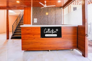 A reception desk with a wooden finish, a ceiling fan, and a patterned wall in the background. - Collection O Khoni Taloja Bypass (Mumbai)