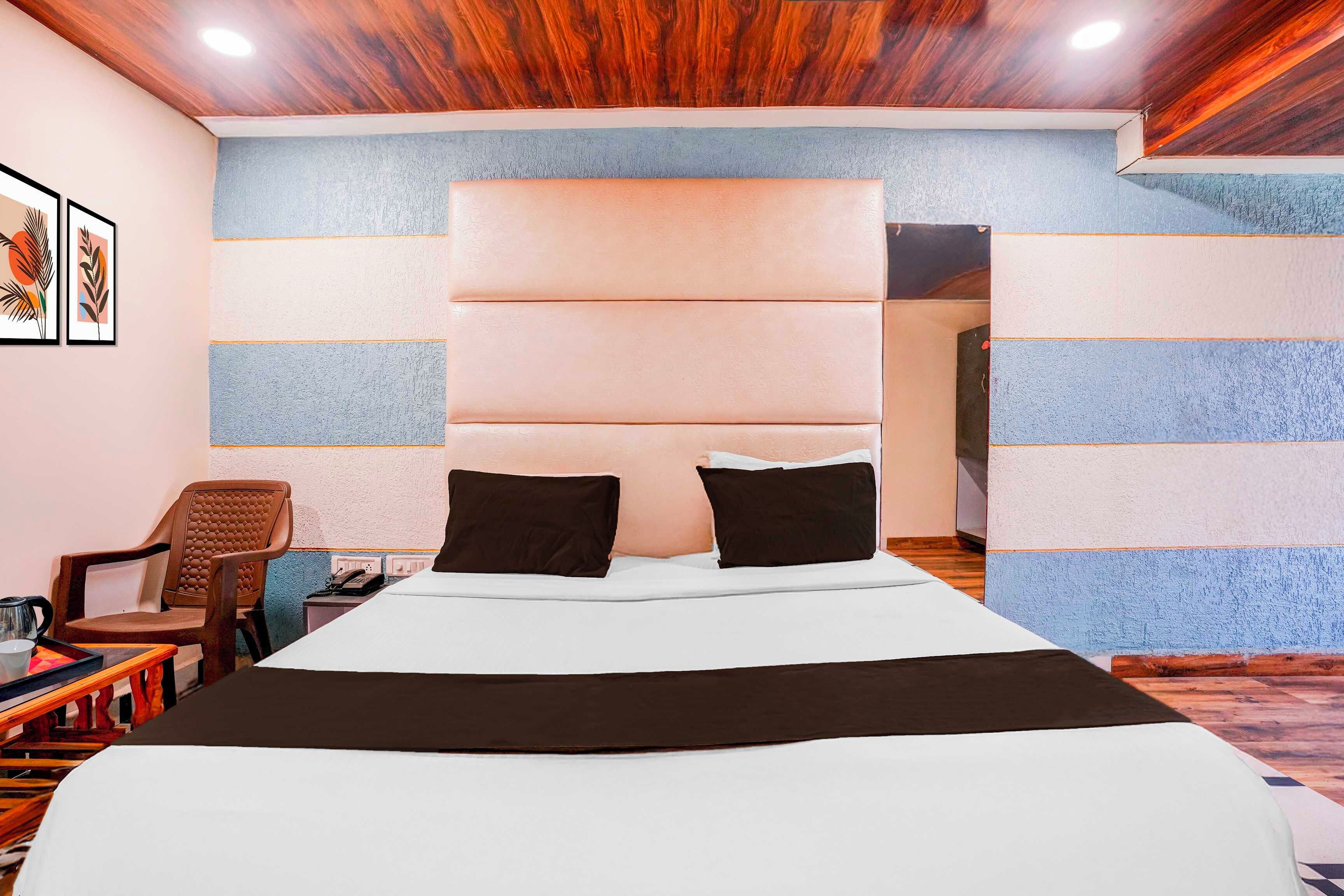 A hotel room with a large bed, a headboard, a chair, a table, and a telephone.