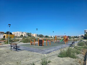 An outdoor playground with various play structures, surrounded by a paved area and a clear sky. - Niki’s Coastal Escape | 2-Bedroom Stay near Mackenzie Beach (Larnaka)