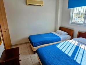 Ein Zimmer mit zwei Betten, einem Holzschrank und einem Fenster mit Jalousien.