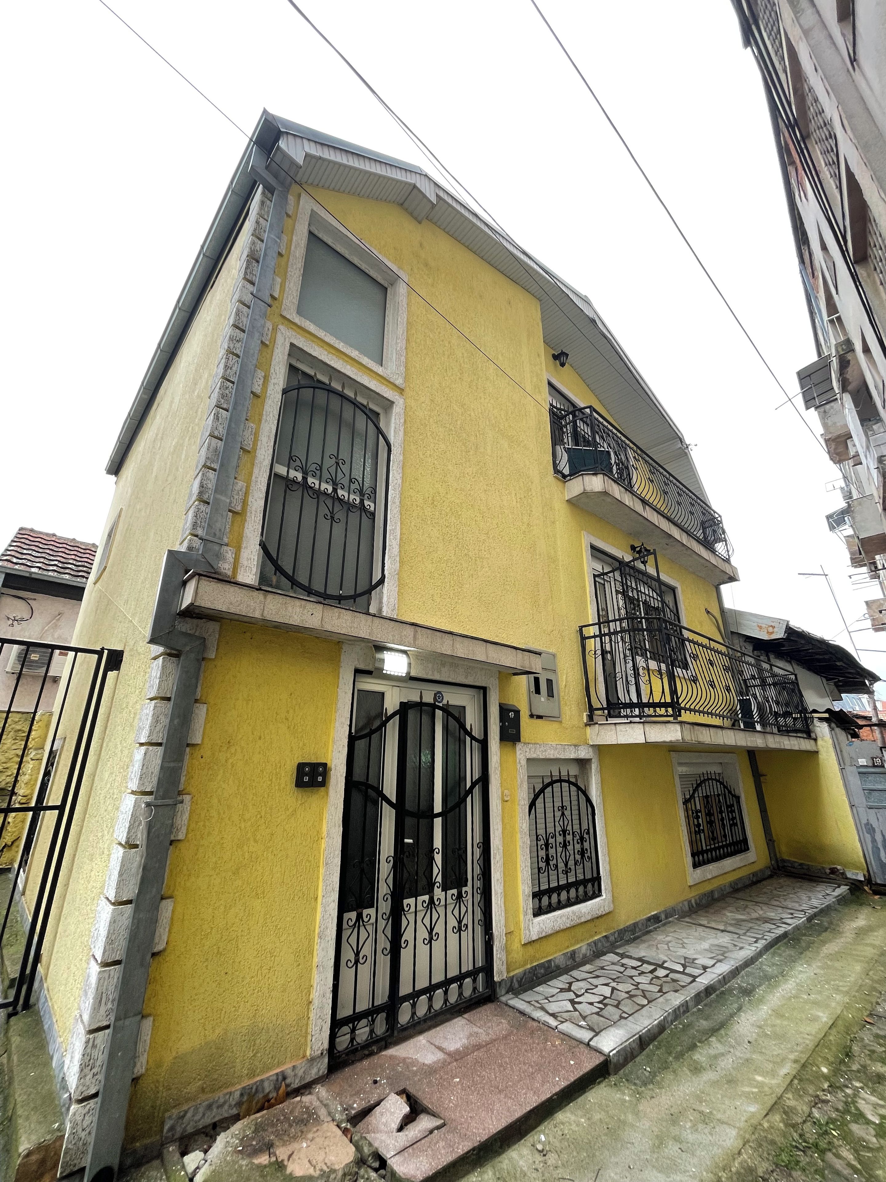 A two-story building with a yellow facade, black metal gates, and a small front porch.