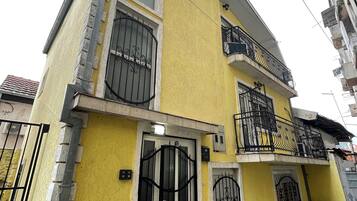 A two-story building with a yellow facade, black metal gates, and a small front porch.