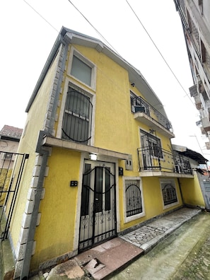 A two-story building with a yellow facade, black metal gates, and a small front porch.