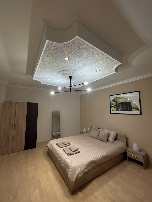 A bedroom with a large bed, a wardrobe, a ceiling light fixture, and a framed picture on the wall.