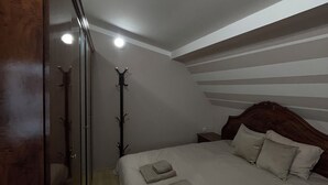 A bedroom with a sloped ceiling, a wooden wardrobe, a bed with pillows and folded towels, and a coat rack. - Central Charm Residence Kumanovo (Kumanovo)