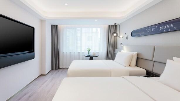 Ein Hotelzimmer mit einem großen Flachbildfernseher, einem Bett mit weißer Bettwäsche, einem kleinen Tisch mit einer Pflanze und einem an der Wand befestigten Schild.