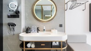 Un baño moderno con un espejo redondo, un perchero para toallas, un secador de pelo y un lavabo con dispensador de jabón.
