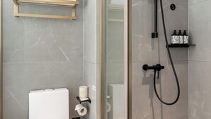Ein modernes Badezimmer mit einer begehbaren Glasdusche, einer Toilette, einem Handtuchhalter und einem Ablagefach für Pflegeutensilien.