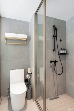 Et stilfuldt badeværelse med et glasvægshus, toilet, et håndklædestativ og en hylde med toiletartikler.