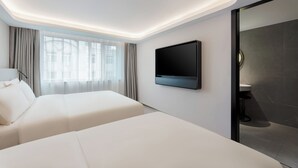 Ein modernes Hotelzimmer mit einem Bett, einem an der Wand befestigten Fernseher und einem Badezimmer mit dunklen Fliesen.