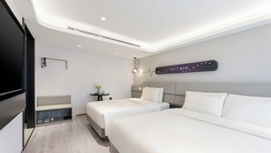 Ein modernes Hotelzimmer mit zwei Betten, einer Sitzecke, einem kleinen Tisch mit Pflanze und einem an der Wand befestigten Schild.