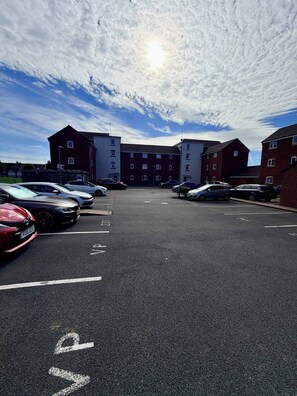 Un parking rempli de voitures et, au fond, un bâtiment à la façade rouge.