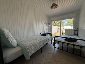 Quarto com duas camas, uma com cabeceira e outra sem, janela com vista para o exterior e luminária pendente.