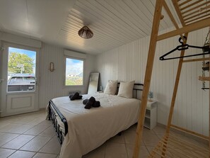 Ein Schlafzimmer mit einem Bett, einer Holzleiter, einem Kleiderständer und einem Fenster mit Blick auf ein Auto und Bäume.