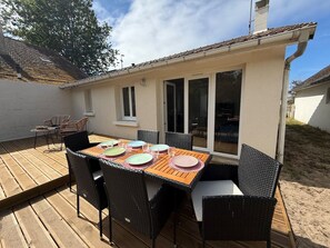 Eine Terrasse im Freien mit Holzdeck, einem Esstisch und Korbstühlen.