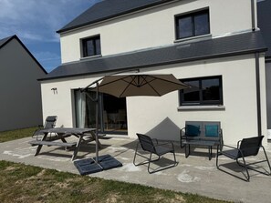 A modern house with a patio area featuring outdoor furniture and a large umbrella. - Contemporary villa near the beaches of the Cotentin Peninsula (Saint-Germain-sur-Ay)