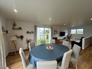 A spacious living area with a round dining table, white chairs, a sofa, and a TV mounted on the wall. - Contemporary villa near the beaches of the Cotentin Peninsula (Saint-Germain-sur-Ay)