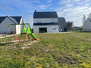 A residential area with a grassy lawn, a swing set, and a modern two-story house with a dark roof. - Contemporary villa near the beaches of the Cotentin Peninsula (Saint-Germain-sur-Ay)