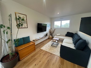 A modern living room with a wooden floor, a sofa set, a coffee table, a TV, and a potted plant. - Contemporary villa near the beaches of the Cotentin Peninsula (Saint-Germain-sur-Ay)