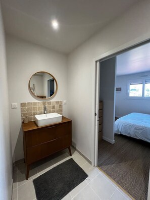 A bathroom with a wooden vanity, a round mirror, and a white sink. - Contemporary villa near the beaches of the Cotentin Peninsula (Saint-Germain-sur-Ay)