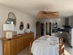 Ein Essbereich mit einem Holzbüfett, einem für eine Mahlzeit gedeckten weißen Tisch und einer Küche im Hintergrund.