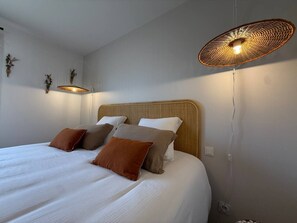 Ein ordentlich bezogenes Bett mit weißer und brauner Bettwäsche, ein Holz-Kopfteil und eine gewebte Leuchte darüber.