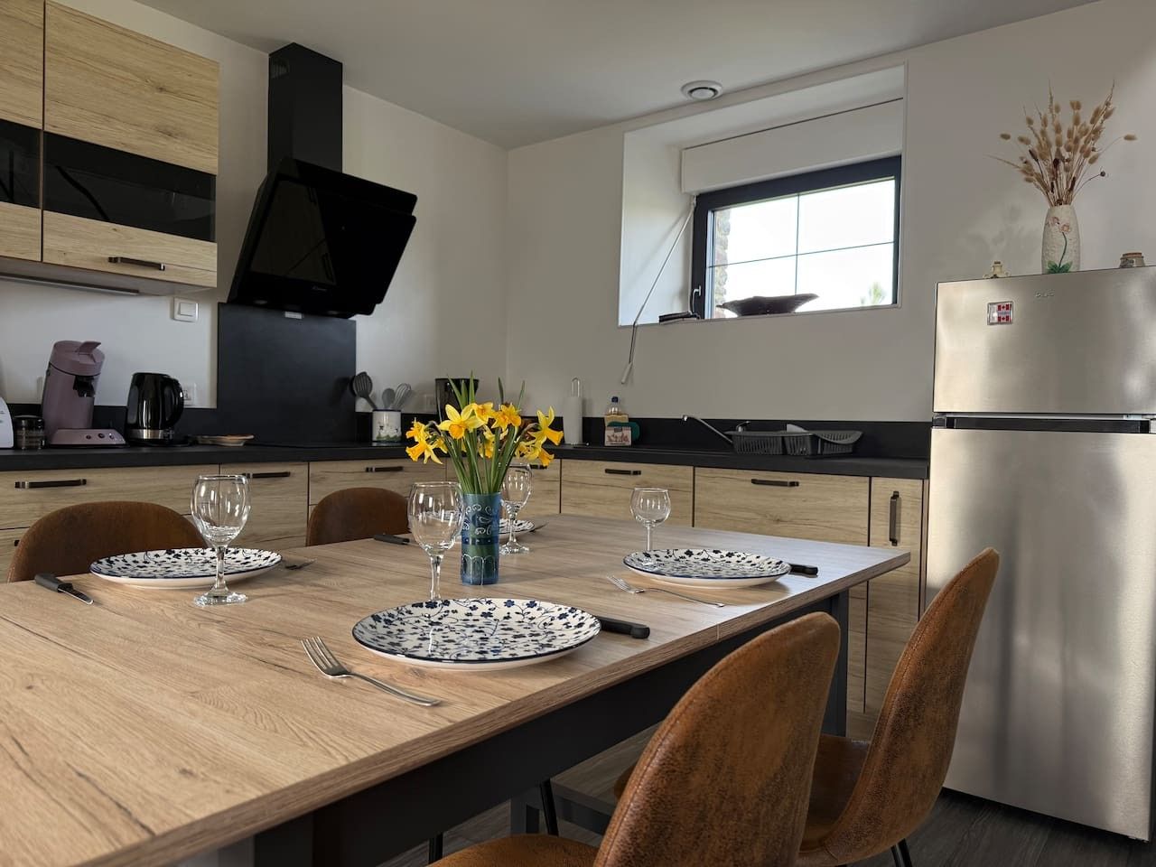A modern kitchen with a dining table set for two, equipped with a refrigerator, stove, and various kitchen appliances.
