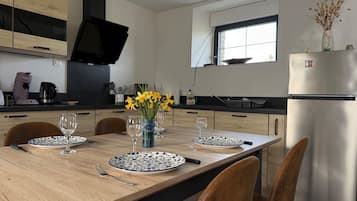 A modern kitchen with a dining table set for two, equipped with a refrigerator, stove, and various kitchen appliances.